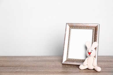 Photo of Photo frame and adorable toy bunny on table against light background, space for text. Child room elements