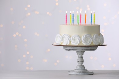 Photo of Birthday cake with burning candles on white table against blurred festive lights, space for text