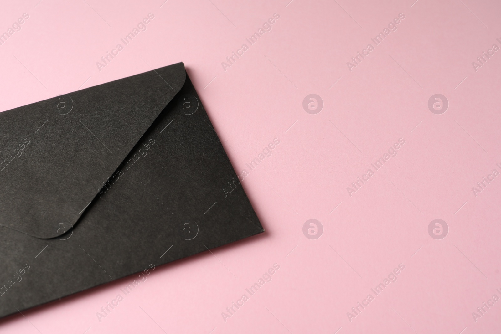 Photo of Black paper envelope on pink background, closeup. Space for text