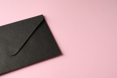 Black paper envelope on pink background, closeup. Space for text