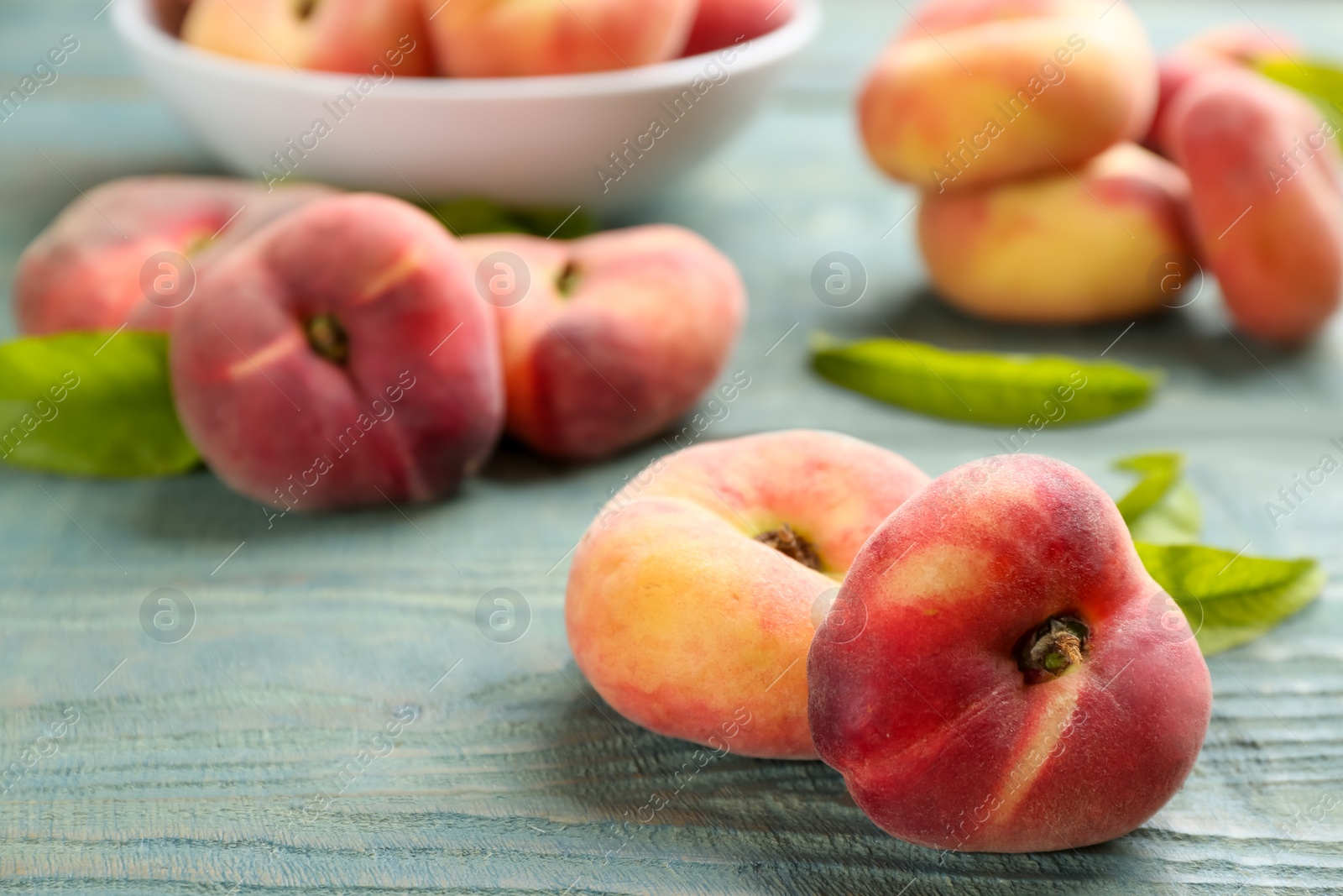 Photo of Fresh ripe donut peaches on light blue wooden table, closeup. Space for text
