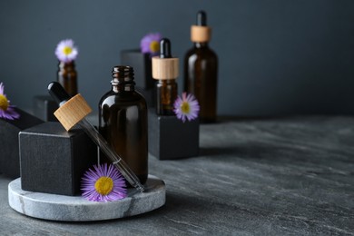 Photo of Bottles of essential oil and beautiful flowers on dark gray stone table, space for text