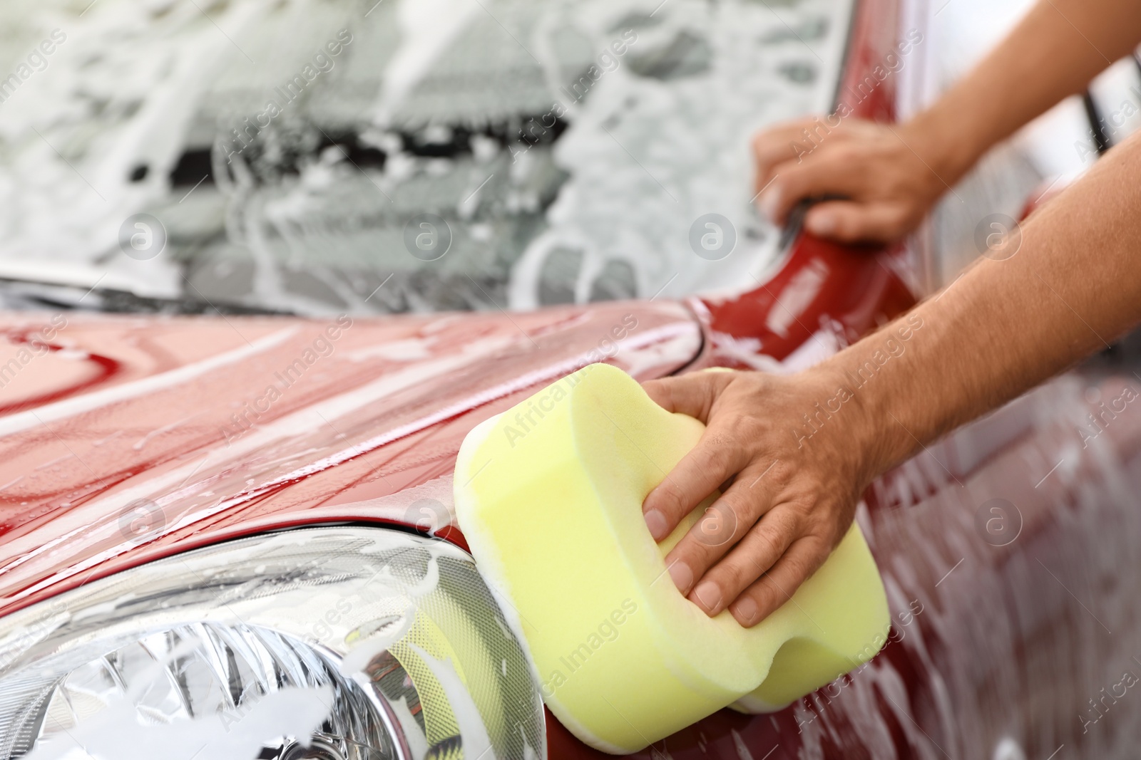 Photo of Man washing red auto with sponge at car wash, closeup