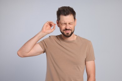 Photo of Man cleaning ears and suffering from pain on grey background