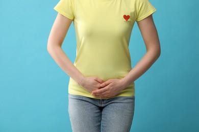 Woman suffering from cystitis on light blue background, closeup