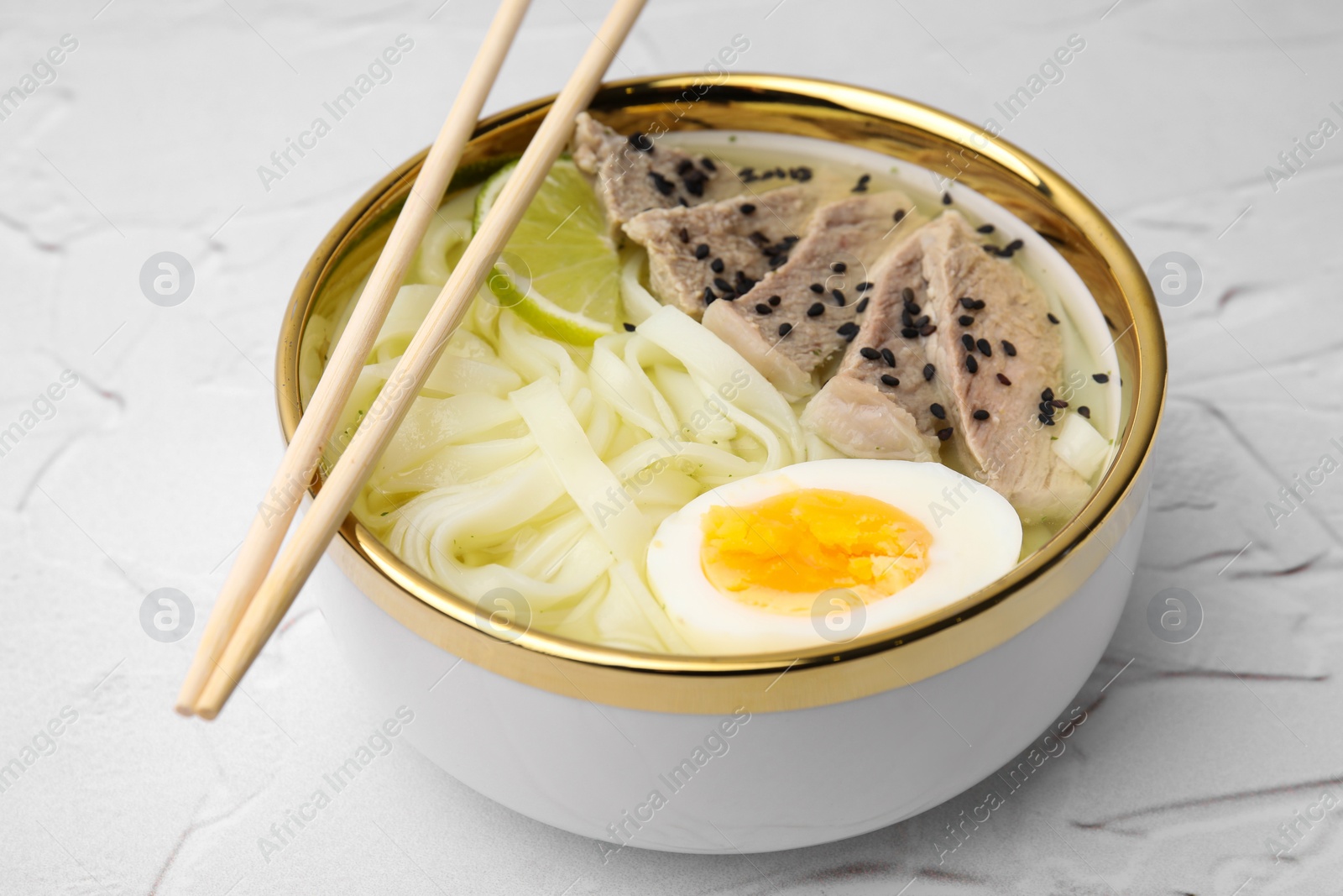 Photo of Bowl of delicious rice noodle soup with meat and egg on white textured table, closeup