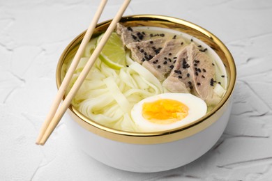 Bowl of delicious rice noodle soup with meat and egg on white textured table, closeup
