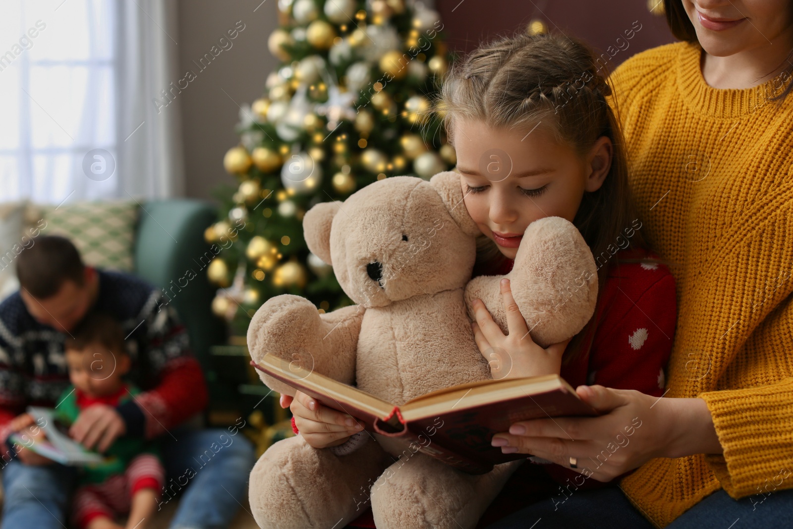 Photo of Mother with her cute daughter reading book in room decorated for Christmas