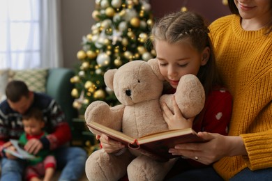 Mother with her cute daughter reading book in room decorated for Christmas