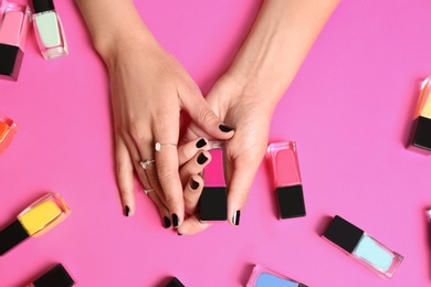 Woman with black manicure holding nail polish bottle on color background, top view