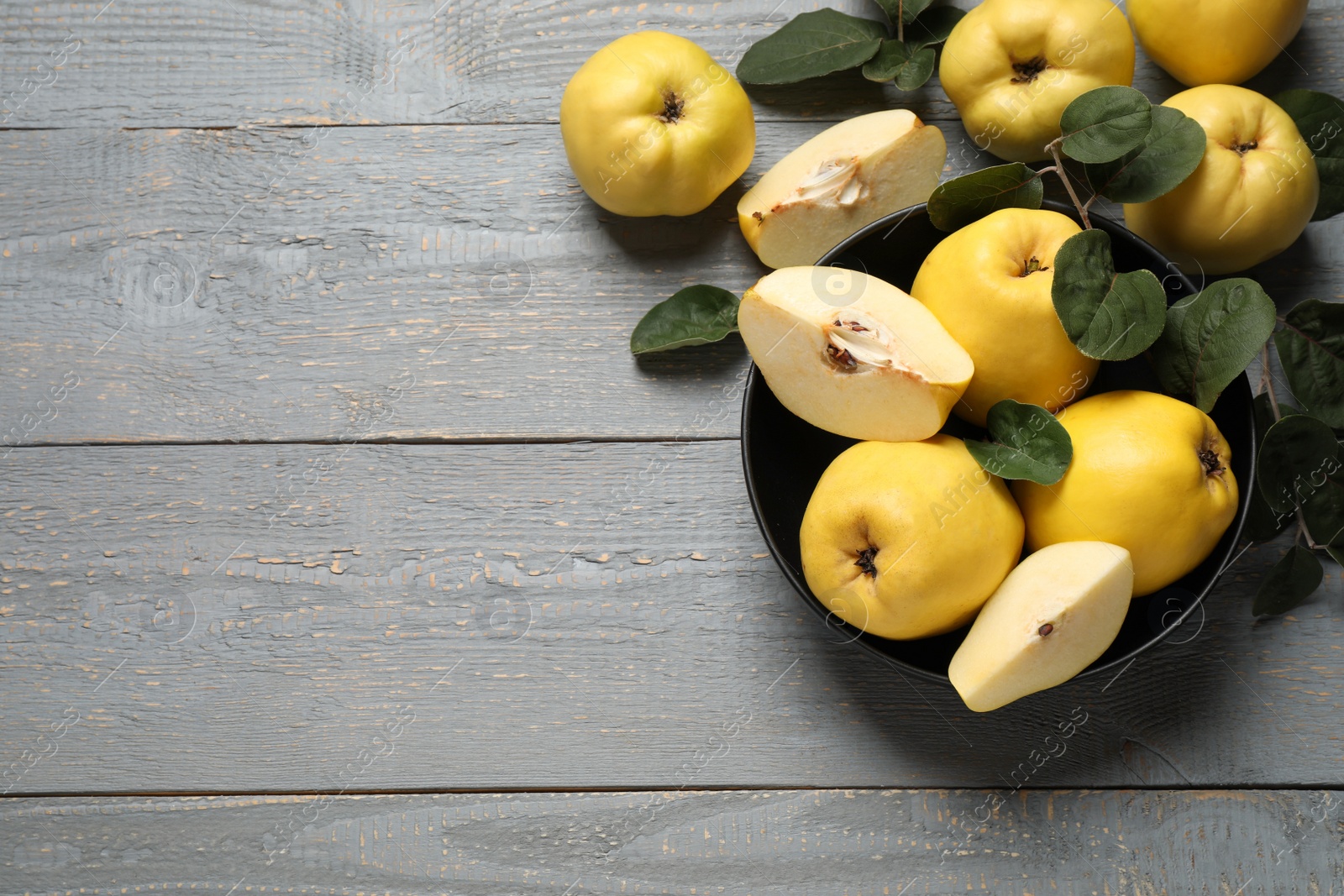 Photo of Fresh ripe organic quinces with leaves on grey wooden table, flat lay. Space for text