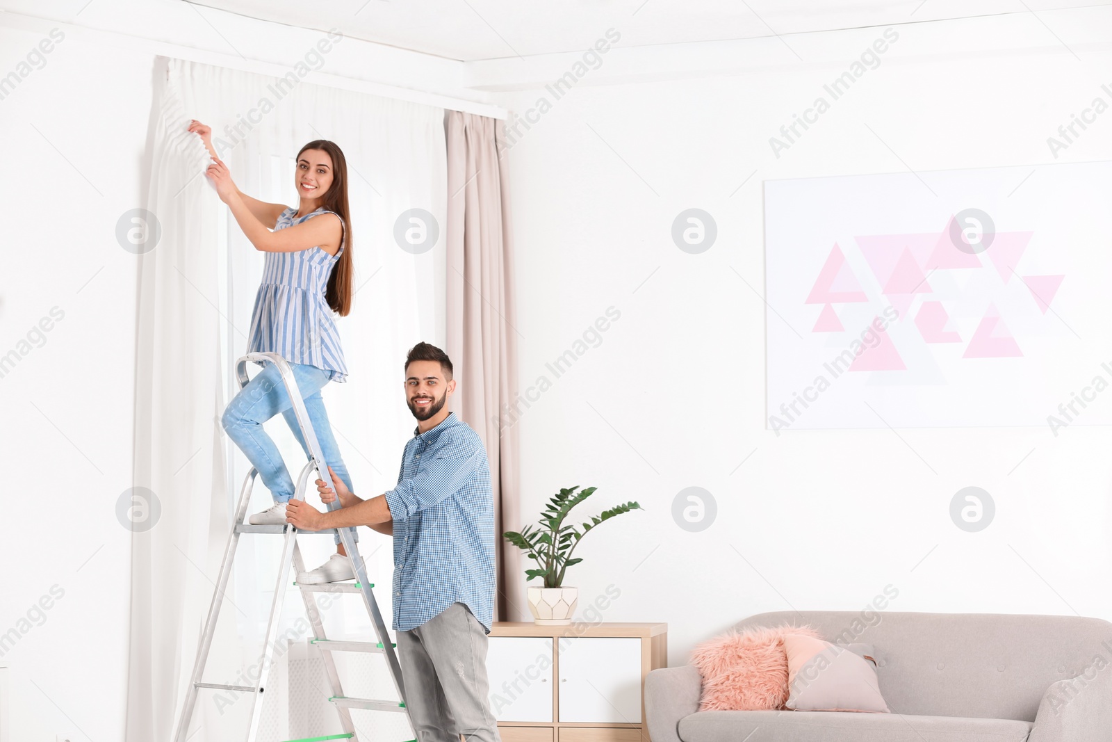 Photo of Young couple hanging window curtain in room. Space for text