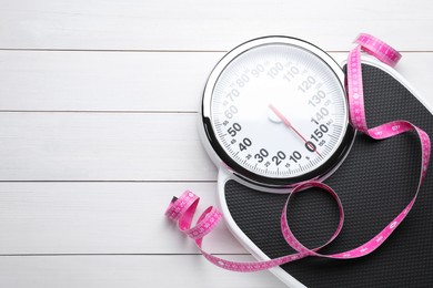 Bathroom scale, measuring tape and space for text on white wooden floor, top view. Weight loss concept