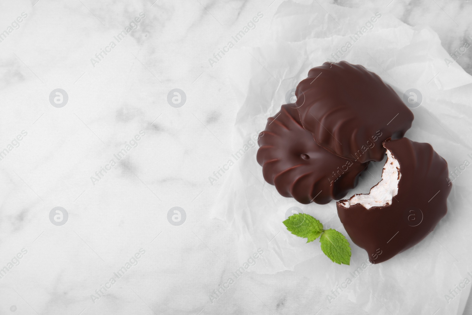 Photo of Delicious chocolate covered marshmallows with mint on white marble table, flat lay. Space for text