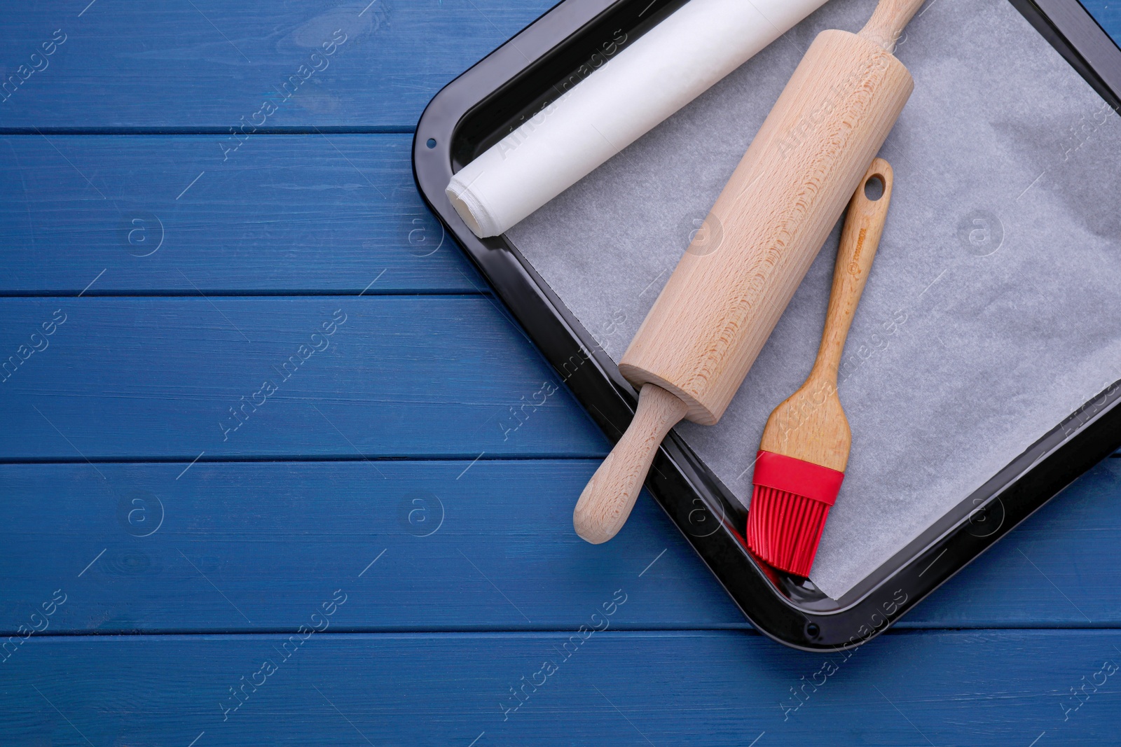 Photo of Baking parchment papers, rolling pin and brush on blue wooden table, flat lay. Space for text