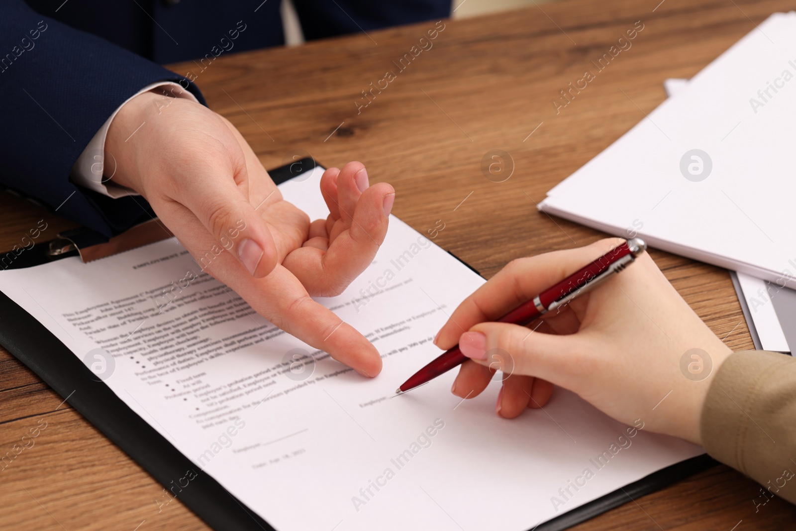 Photo of Man pointing at document and woman putting signature at wooden table, closeup