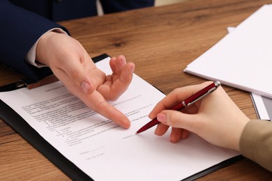 Man pointing at document and woman putting signature at wooden table, closeup