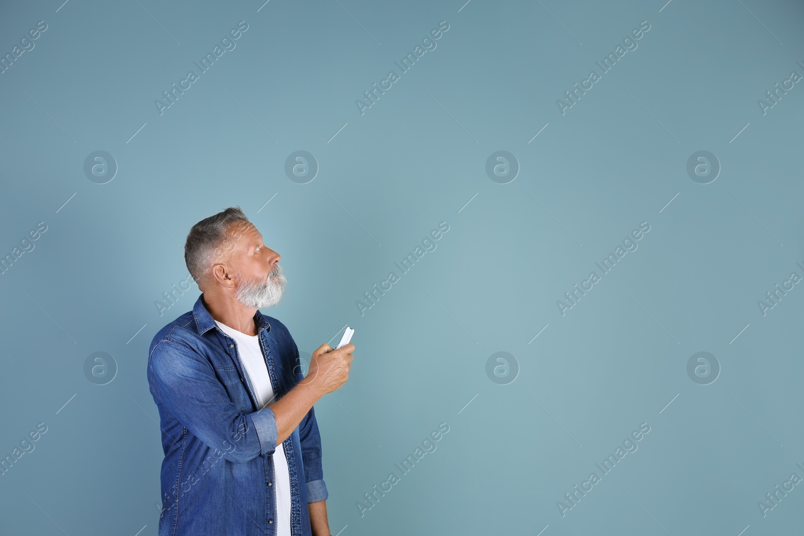 Photo of Senior man with air conditioner remote control on color background