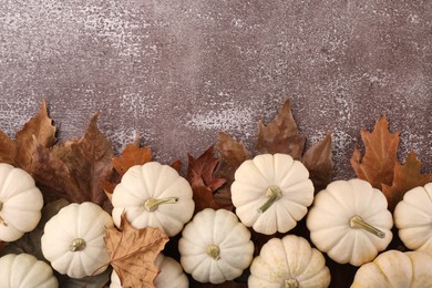 Photo of Ripe white pumpkins and dry leaves on grey textured table, flat lay. Space for text