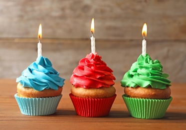 Photo of Delicious birthday cupcakes with candles on table