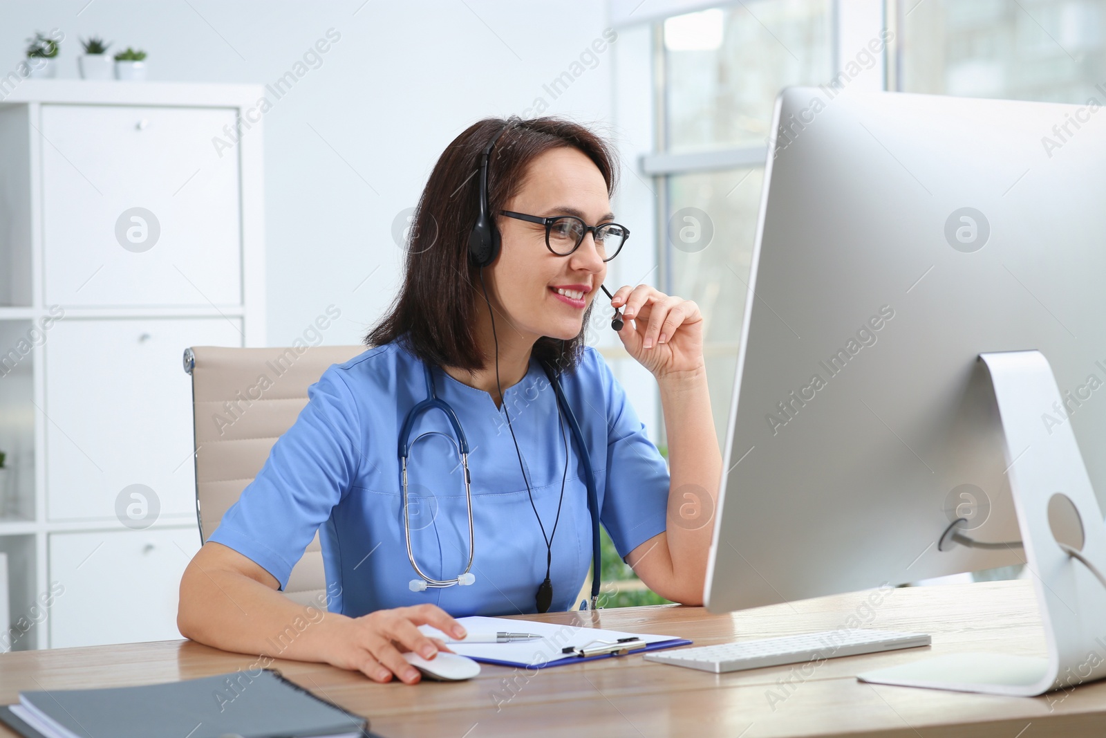 Photo of Doctor with headset and computer consulting patient online in office. Hotline service