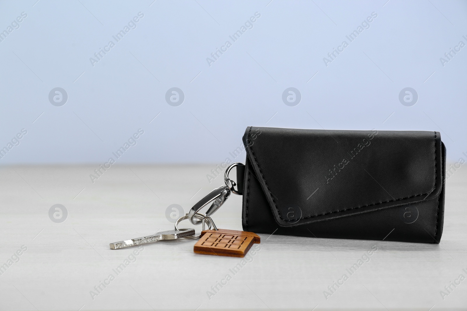 Photo of Leather case with key on white wooden table. Space for text