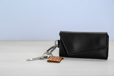 Photo of Leather case with key on white wooden table. Space for text