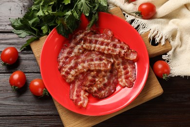 Plate with fried bacon slices, tomatoes and parsley on wooden table, flat lay
