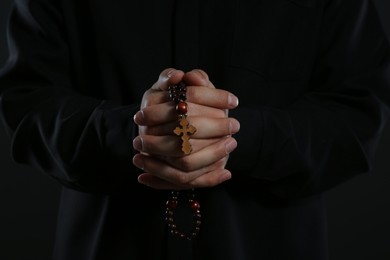 Photo of Priest with rosary beads praying on black background, closeup