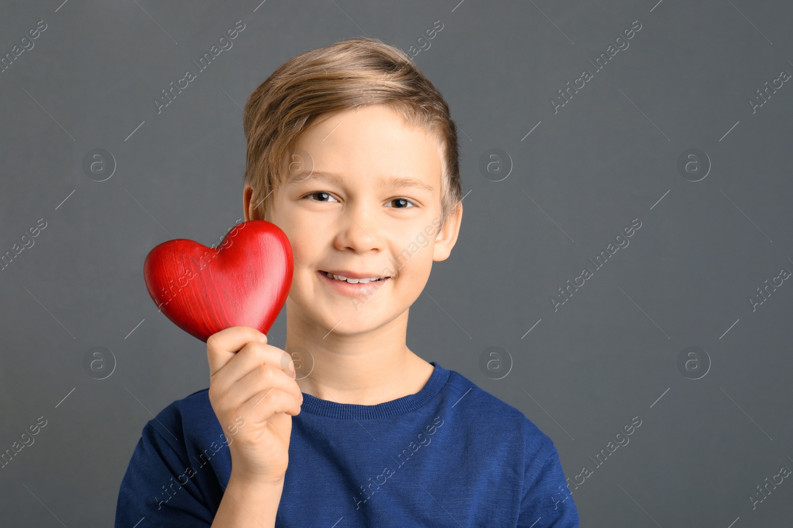 Photo of Cute boy holding wooden heart on grey background. Space for text