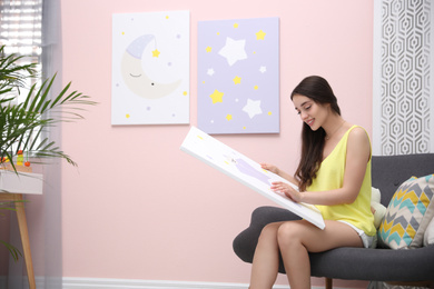 Photo of Decorator with picture sitting near pink wall indoors. Children's room interior design