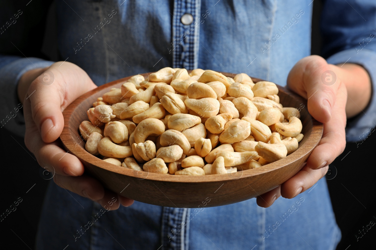 Photo of Woman holding bowl of cashew nuts on black background, closeup