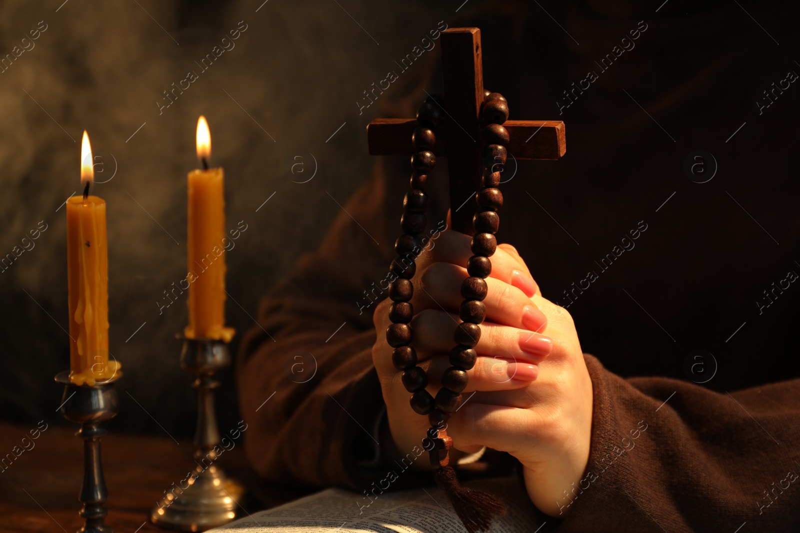 Photo of Woman praying at table with burning candles and cross, closeup