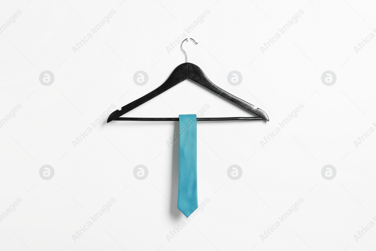 Photo of Hanger with light blue necktie on white wall