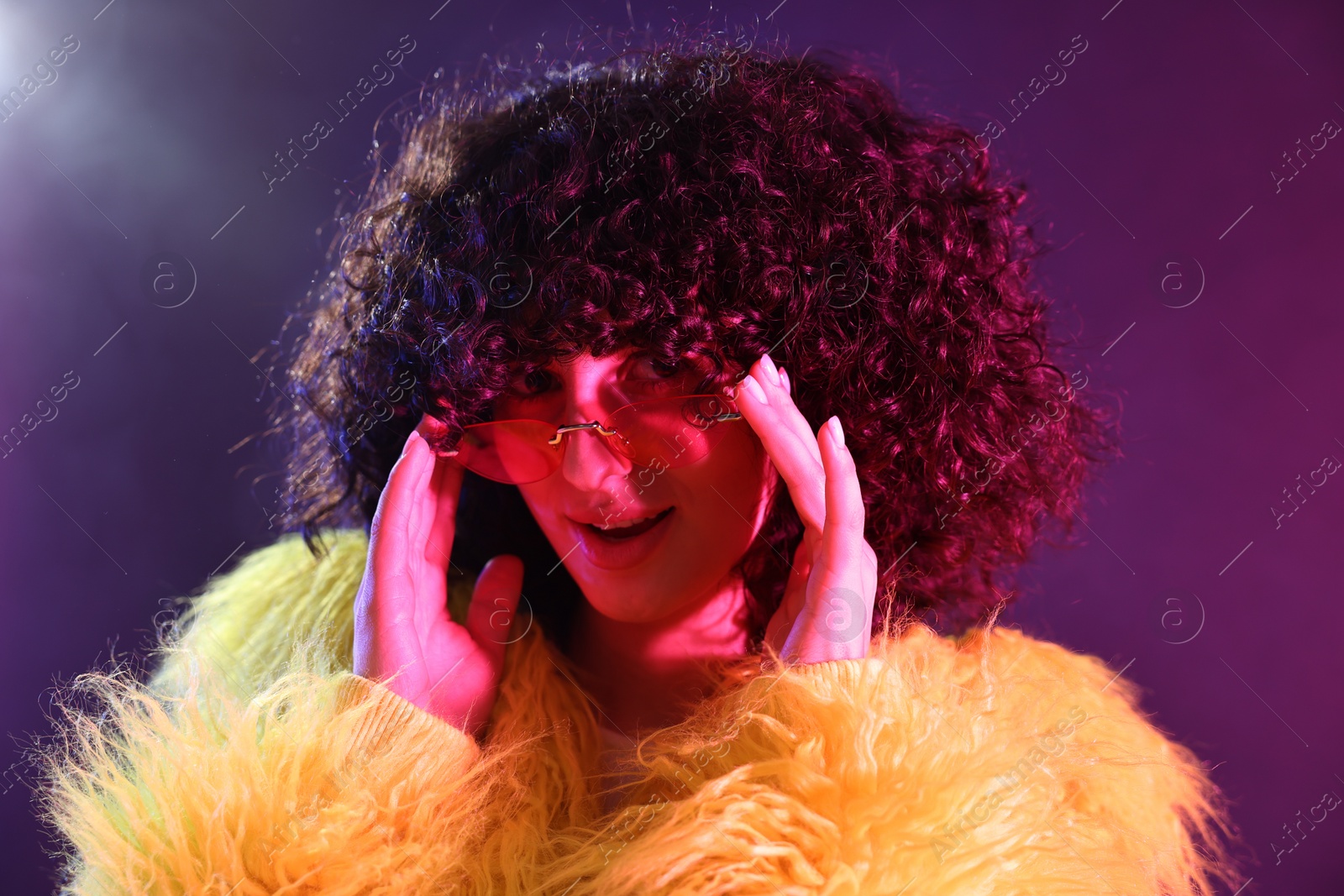 Photo of Beautiful young woman in yellow fur coat and sunglasses on color background in neon lights