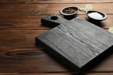 Photo of Black cutting board, salt, pepper and bay leaves on wooden table. Space for text