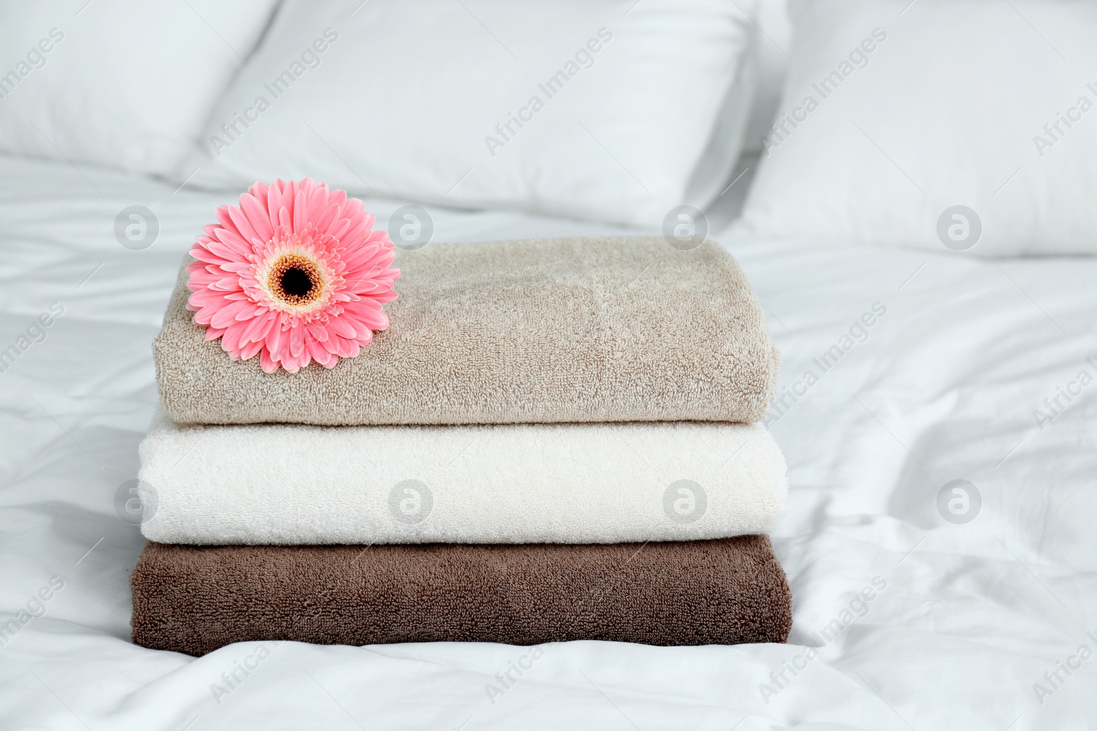 Photo of Stack of clean towels and beautiful gerbera flower on bed