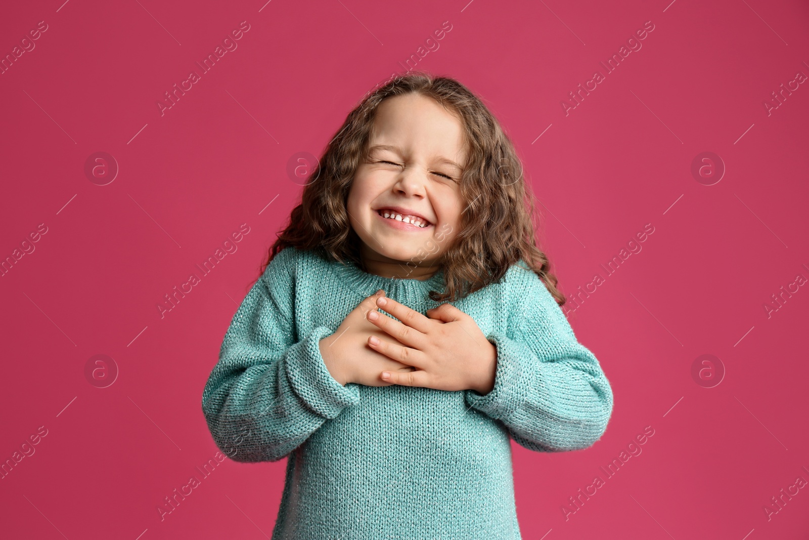 Photo of Cute grateful little girl with hands on chest against pink background