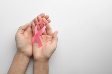 Woman holding pink ribbon on white background, top view with space for text. Breast cancer awareness concept