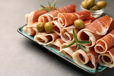 Photo of Rolled slices of delicious jamon with rosemary and olives on grey table, closeup. Space for text