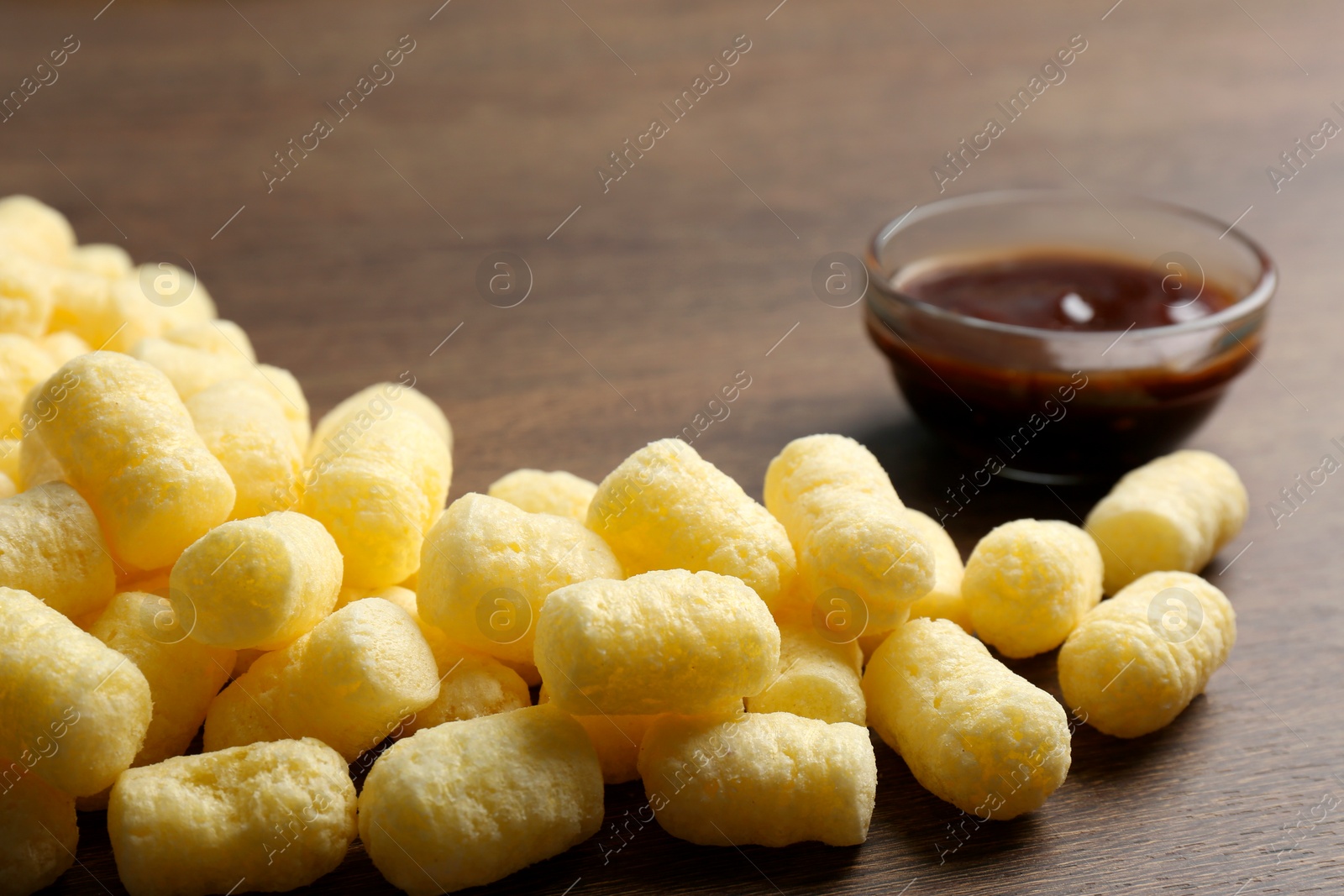 Photo of Delicious crispy corn sticks and bowl of jam on wooden table