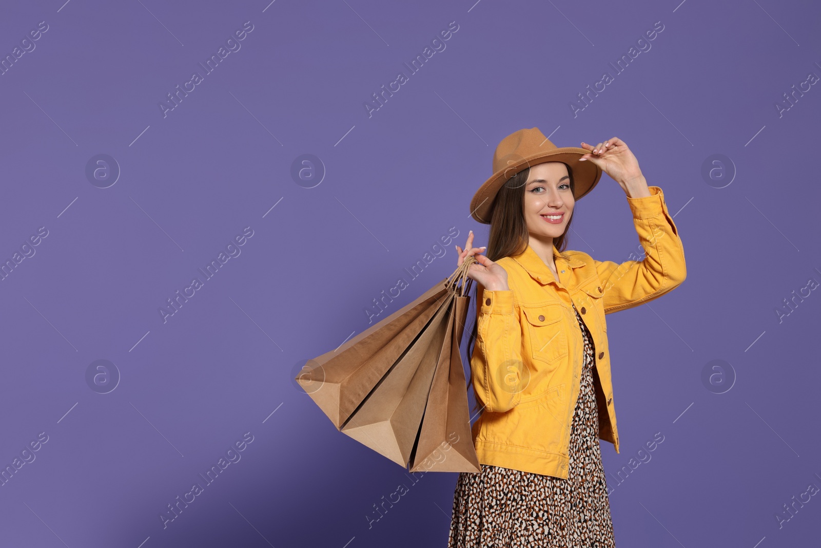 Photo of Stylish young woman with shopping bags on purple background, space for text