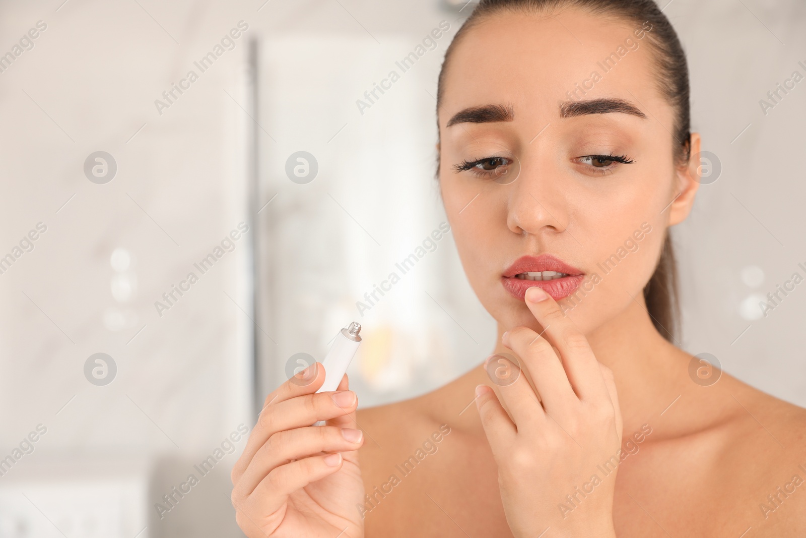 Photo of Woman with herpes applying cream on lips against blurred background. Space for text