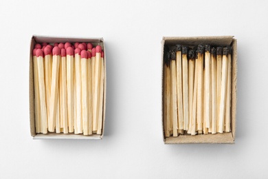 Cardboard boxes with whole and burnt matches on white background, top view