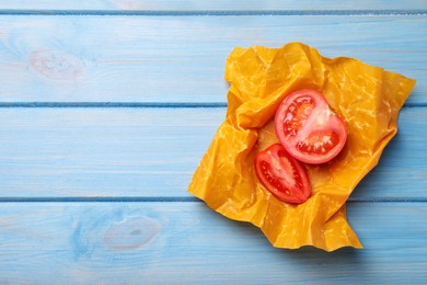 Photo of Slices of fresh tomato in beeswax food wrap on light blue wooden table, top view. Space for text