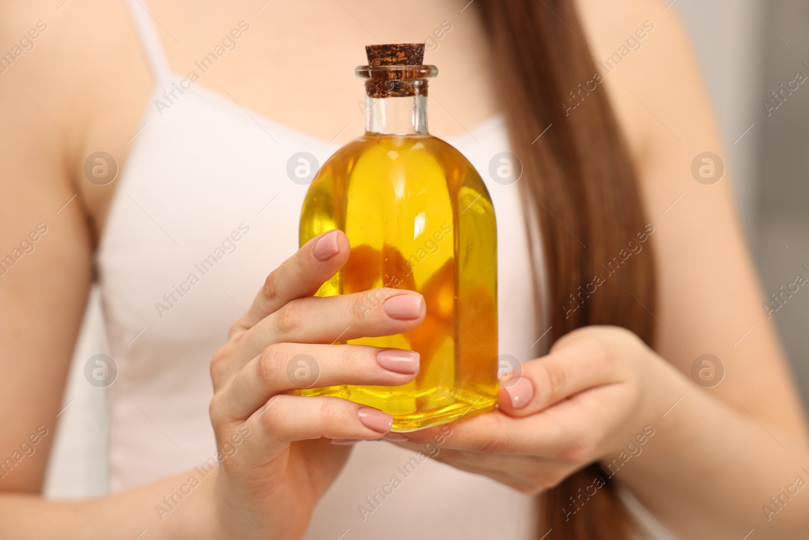 Photo of Natural hair mask. Woman holding bottle of oil at home, closeup