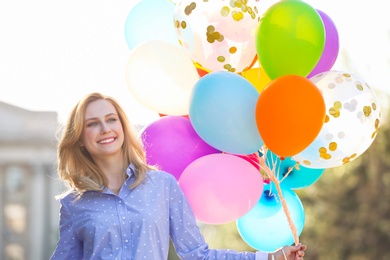 Photo of Young woman with colorful balloons outdoors on sunny day