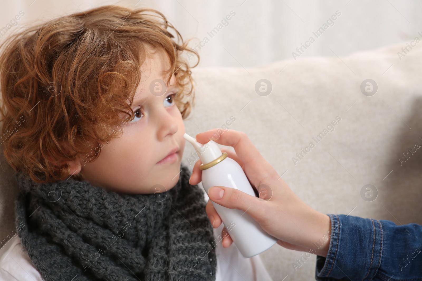 Photo of Mother using nasal spray to treat her little son on sofa, closeup