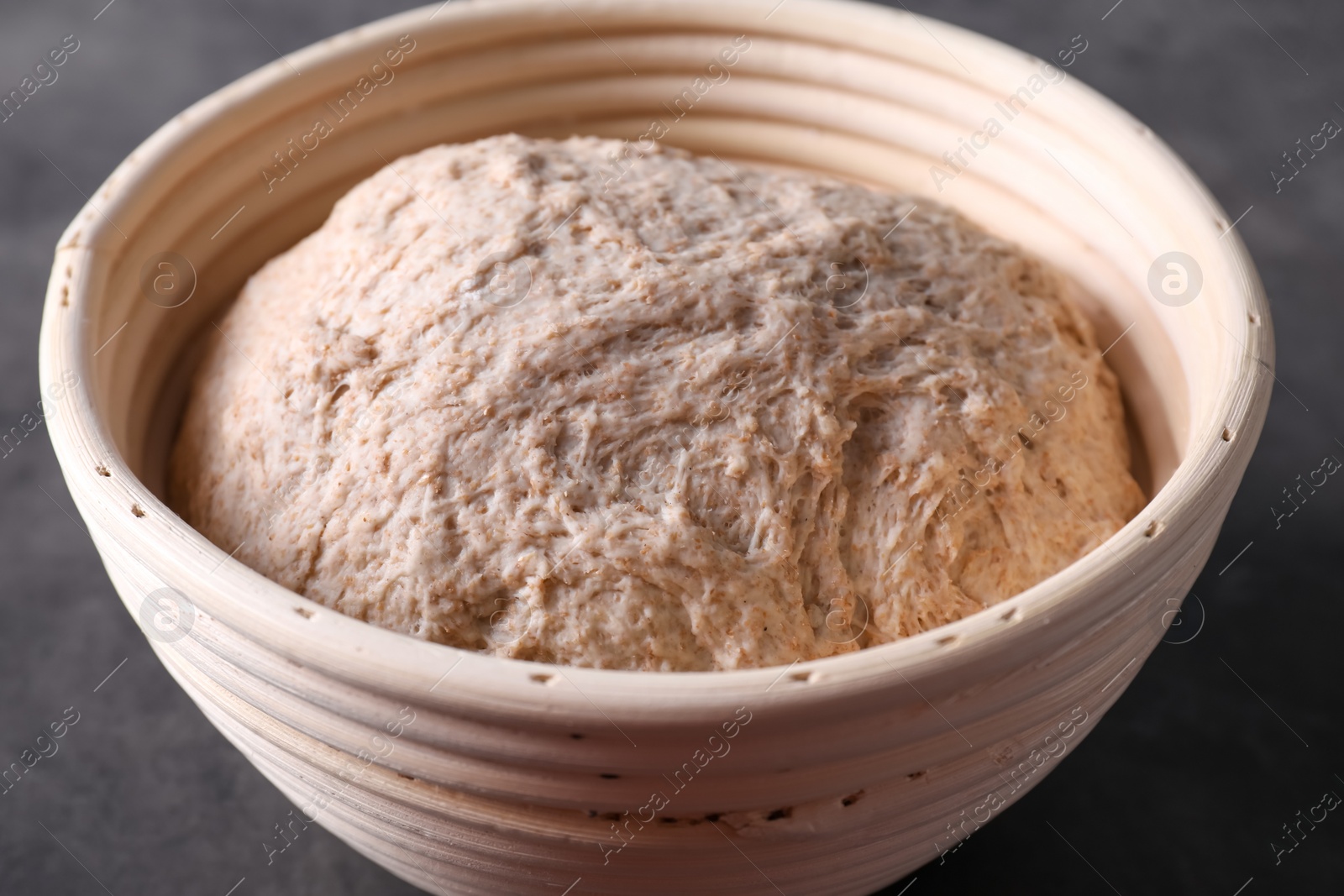 Photo of Fresh sourdough in proofing basket on grey table, closeup