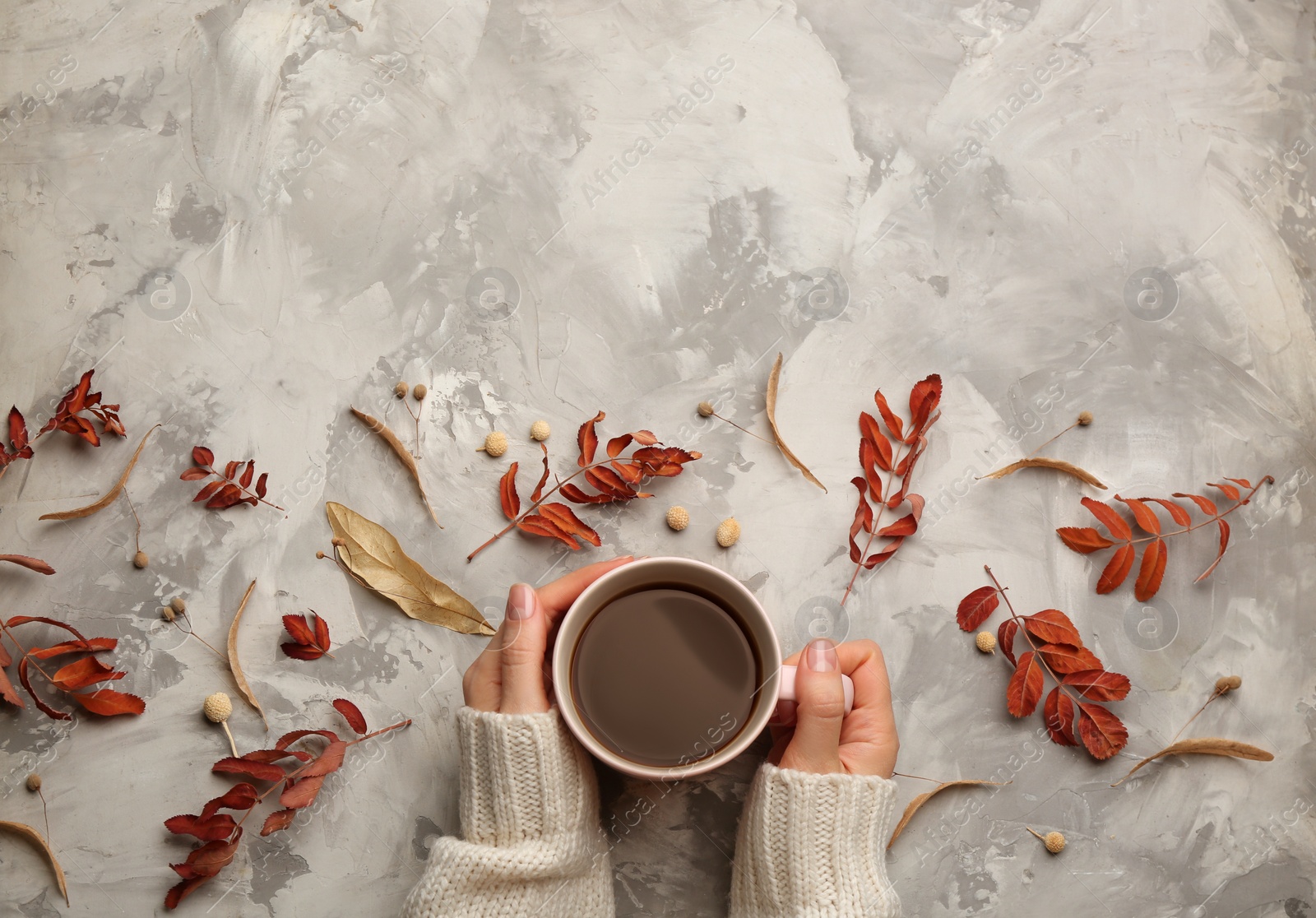 Photo of Woman with cup of hot drink at grey table, top view with space for text. Cozy autumn atmosphere